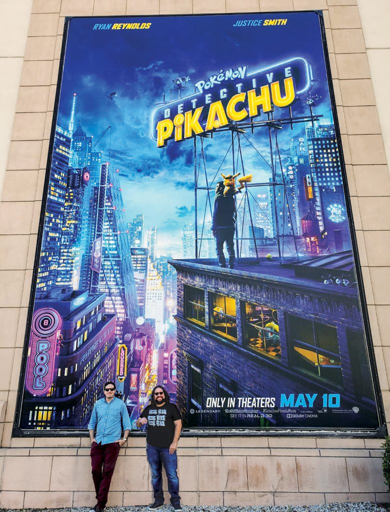 Dan Hernandez ’06 and Benji Samit ’06 standing in front of a Pokémon: Detective Pikachu poster